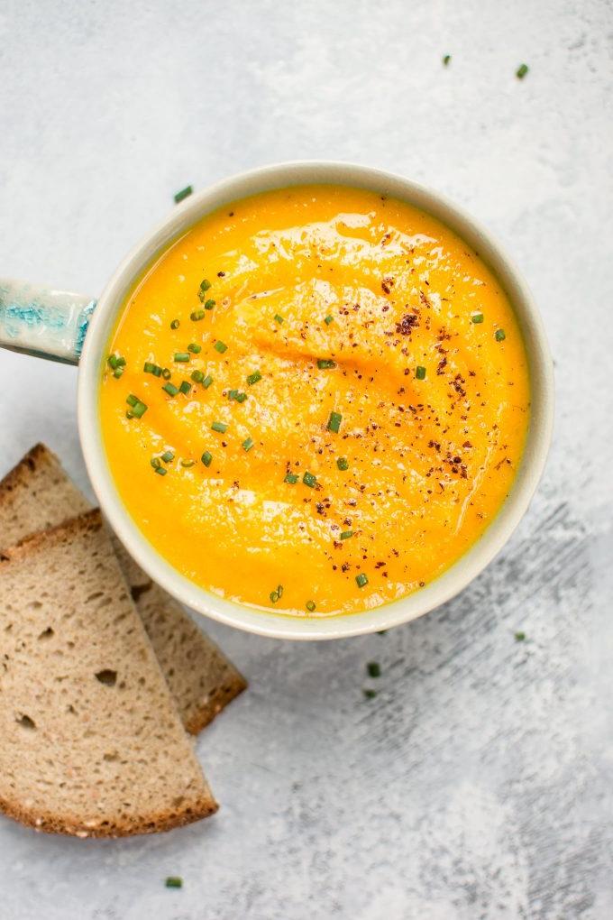 Nahaufnahme von Eichelkürbis-Karotten-Suppe in einer Suppentasse neben Brotscheiben