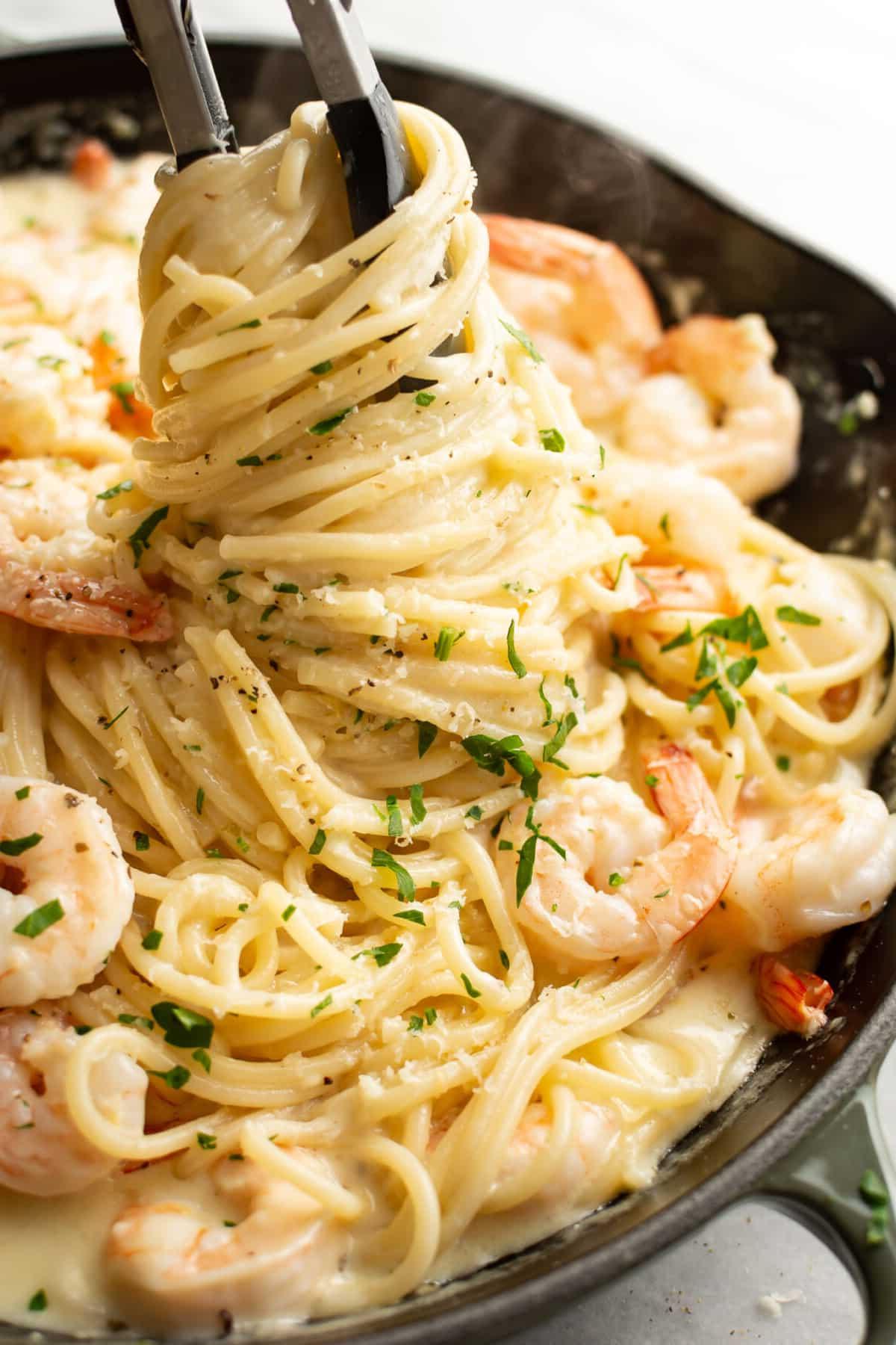 Eine Pfanne mit cremiger Zitronen-Garnelen-Pasta und Kochzangen