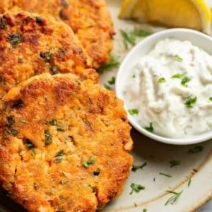 Ein Teller mit drei Lachs-Patties, einer Zitronenspalte und Dip
