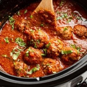 Ein Slow Cooker mit Hackbällchen in Tomatensauce und einem Holzkochlöffel