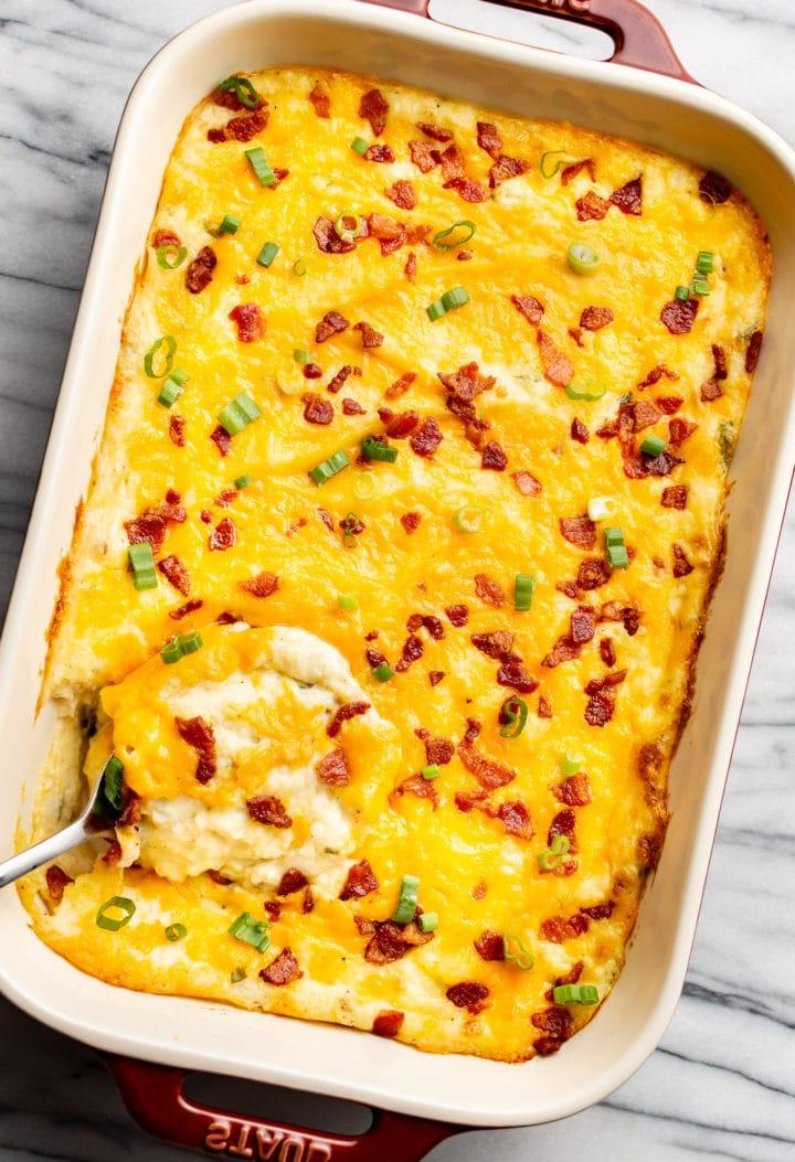 Reichhaltiger Kartoffelpüree-Auflauf 7 a baking dish with cheesy loaded mashed potato casserole and a serving spoon