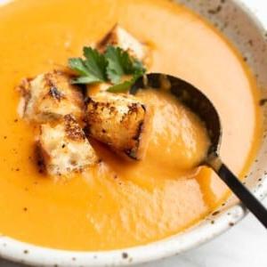 Eine Schüssel Kartoffel-Lauch-Tomaten-Suppe mit Croutons und einem Löffel bereit zum Genießen