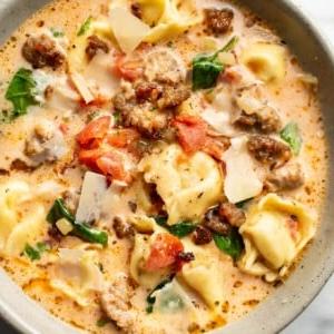Italienische Salsiccia-Tortellini-Suppe 8 Nahaufnahme einer Schale italienischer Wurst-Tortellini-Suppe, garniert mit gehobeltem Parmesan