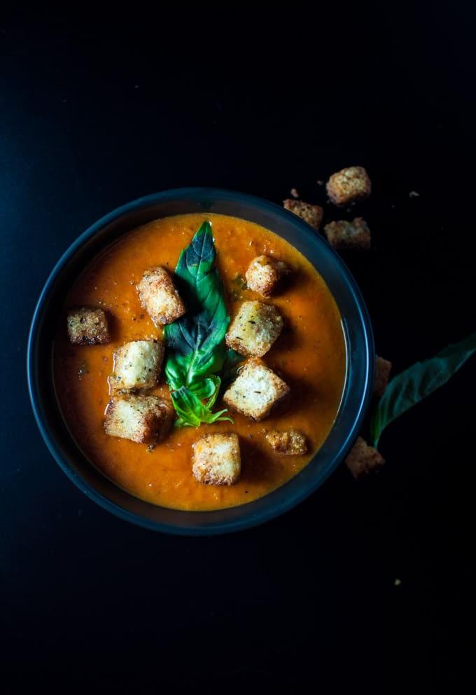 Schwarze Schale einfacher Tomatensuppe, garniert mit Salbei-Croutons und Basilikum