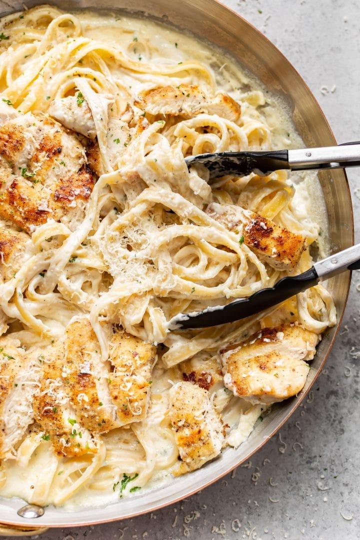 Hähnchen Fettuccine Alfredo 2 Nahaufnahme von Hähnchen Fettuccine Alfredo in einer Pfanne, die mit einer Kochzange gewendet wird
