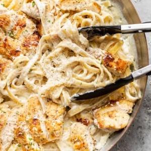 Hähnchen Fettuccine Alfredo 8 Nahaufnahme von Hähnchen Fettuccine Alfredo in einer Pfanne, die mit einer Kochzange gewendet wird