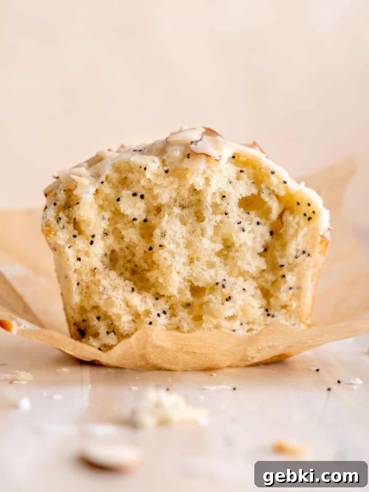 Irresistible Almond Poppy Seed Muffins 6 Half of an almond muffin on a parchment liner showing its fluffy poppy seed-filled inside, ready to be eaten.