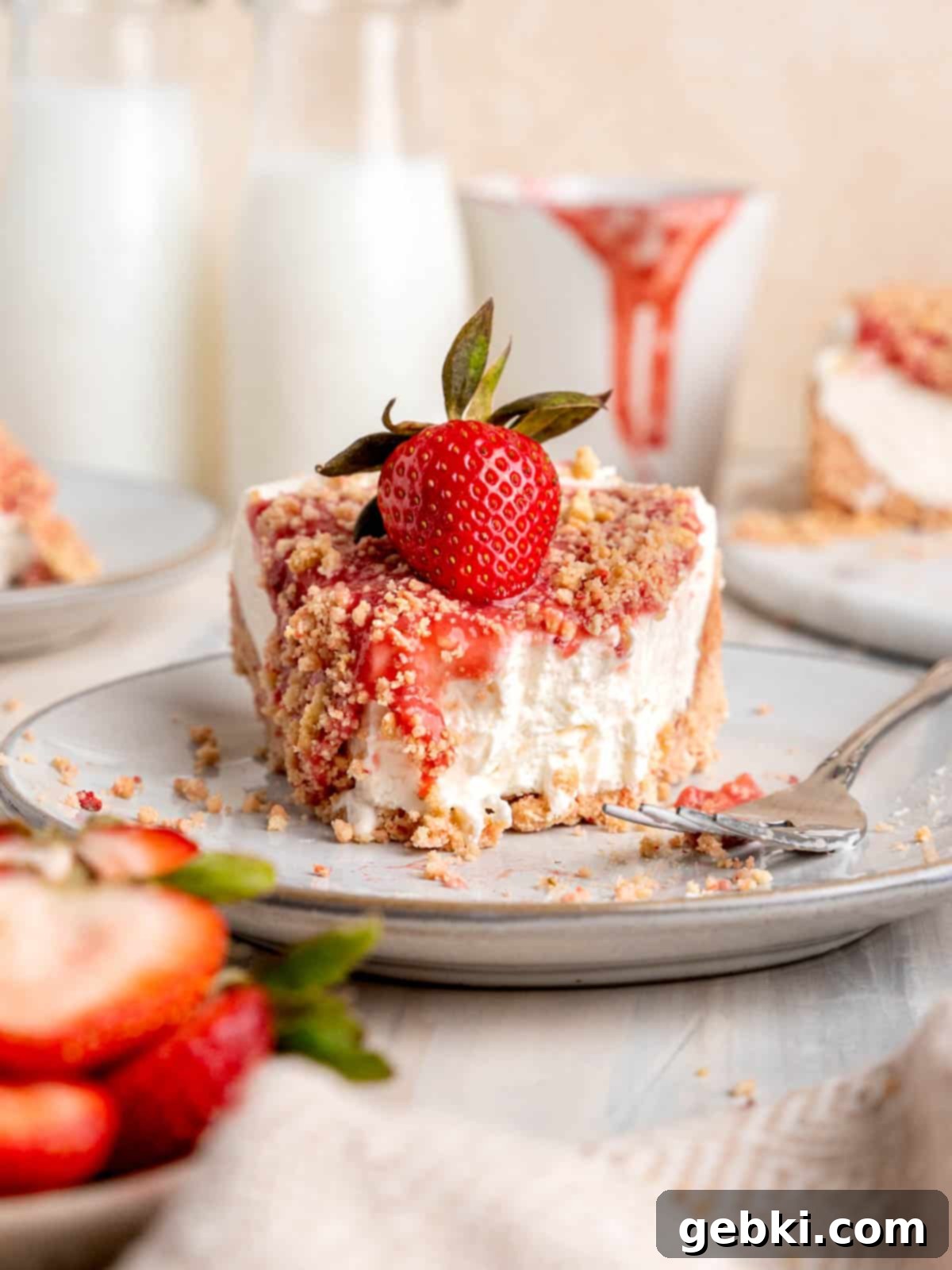 No Bake Strawberry Crunch Cheesecake 12 A perfectly sliced piece of strawberry crunch cheesecake with a bite taken out, showing the layers of crust, creamy filling, and strawberry sauce with crunchy topping.