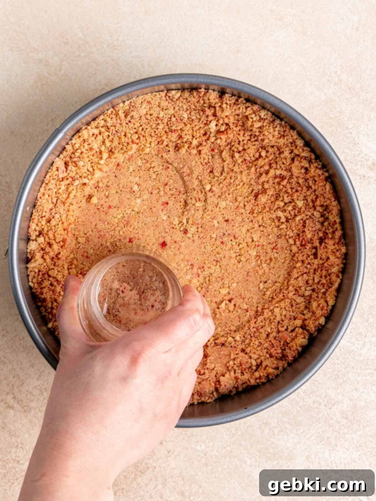 No Bake Strawberry Crunch Cheesecake 5 Strawberry Oreo crust being pressed into the base of a springform pan.