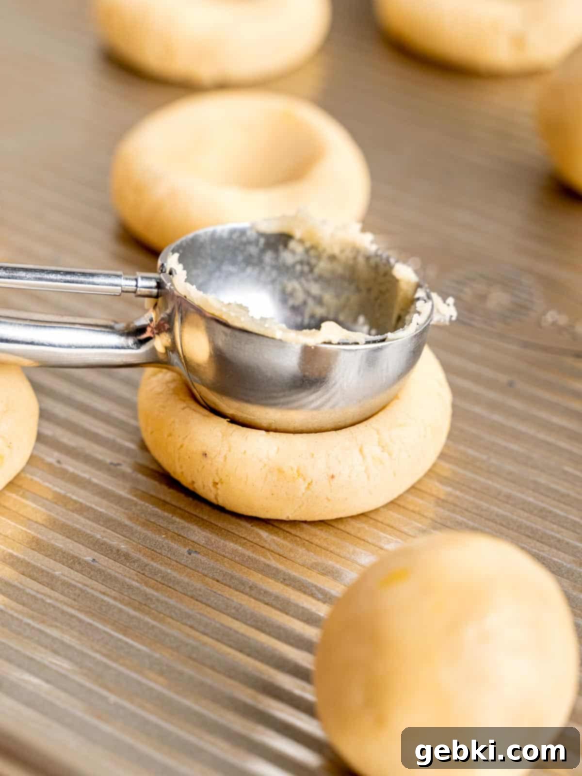 Simple Lemon Curd Thumbprint Cookies 7 Pressing into the center of a cookie dough ball with the back of a cookie scoop.
