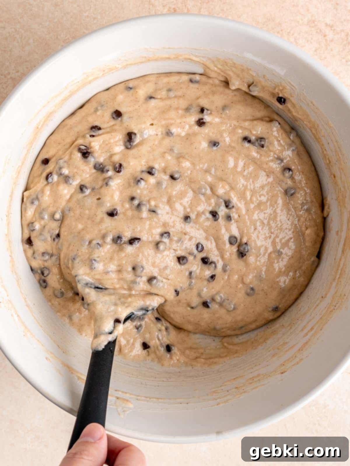 Folding mini chocolate chips into cinnamon muffin batter.