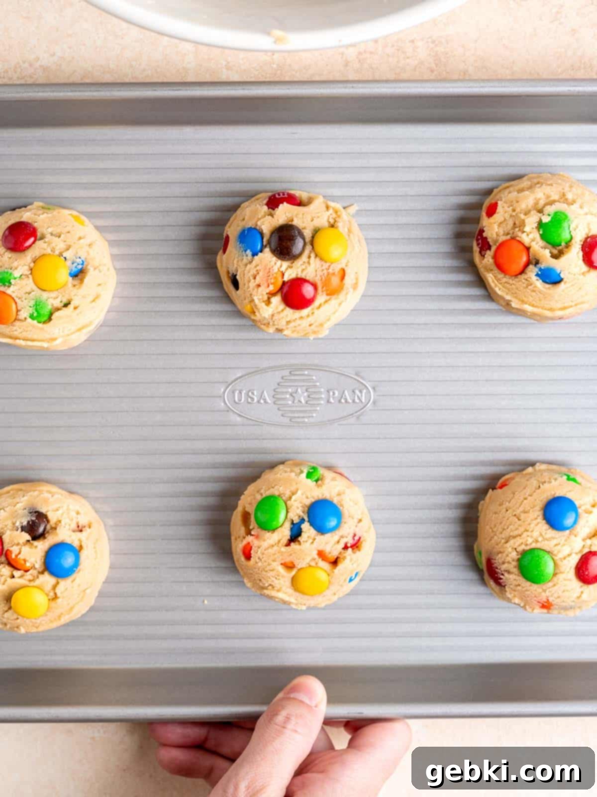 Cookie dough balls with M&Ms placed on a baking sheet, spaced apart for even baking.
