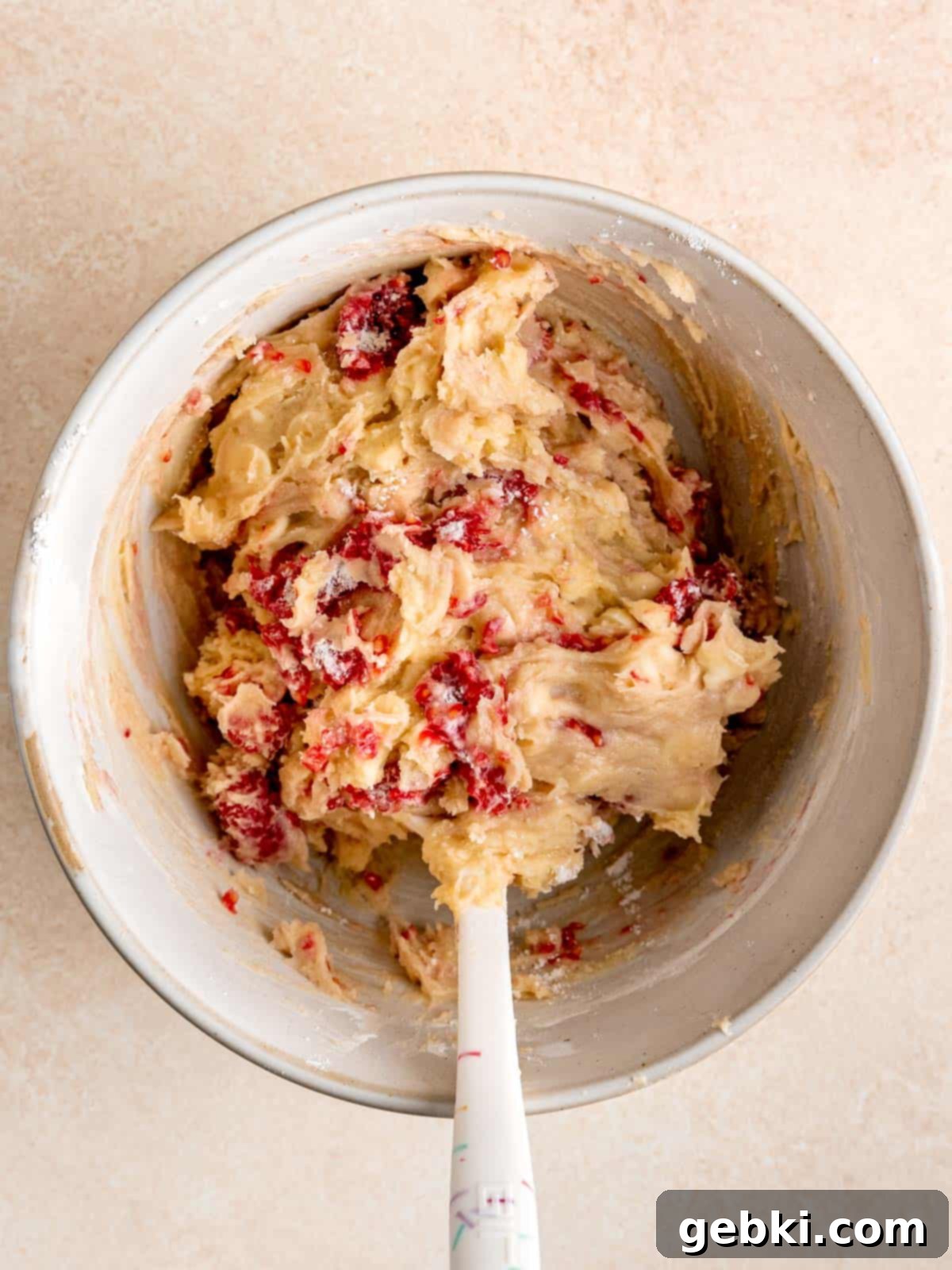 White Chocolate Raspberry Swirl Blondies 6 A spatula gently folding flour-coated raspberries and white chocolate chunks into the thick blondie batter, with a few streaks of flour remaining.