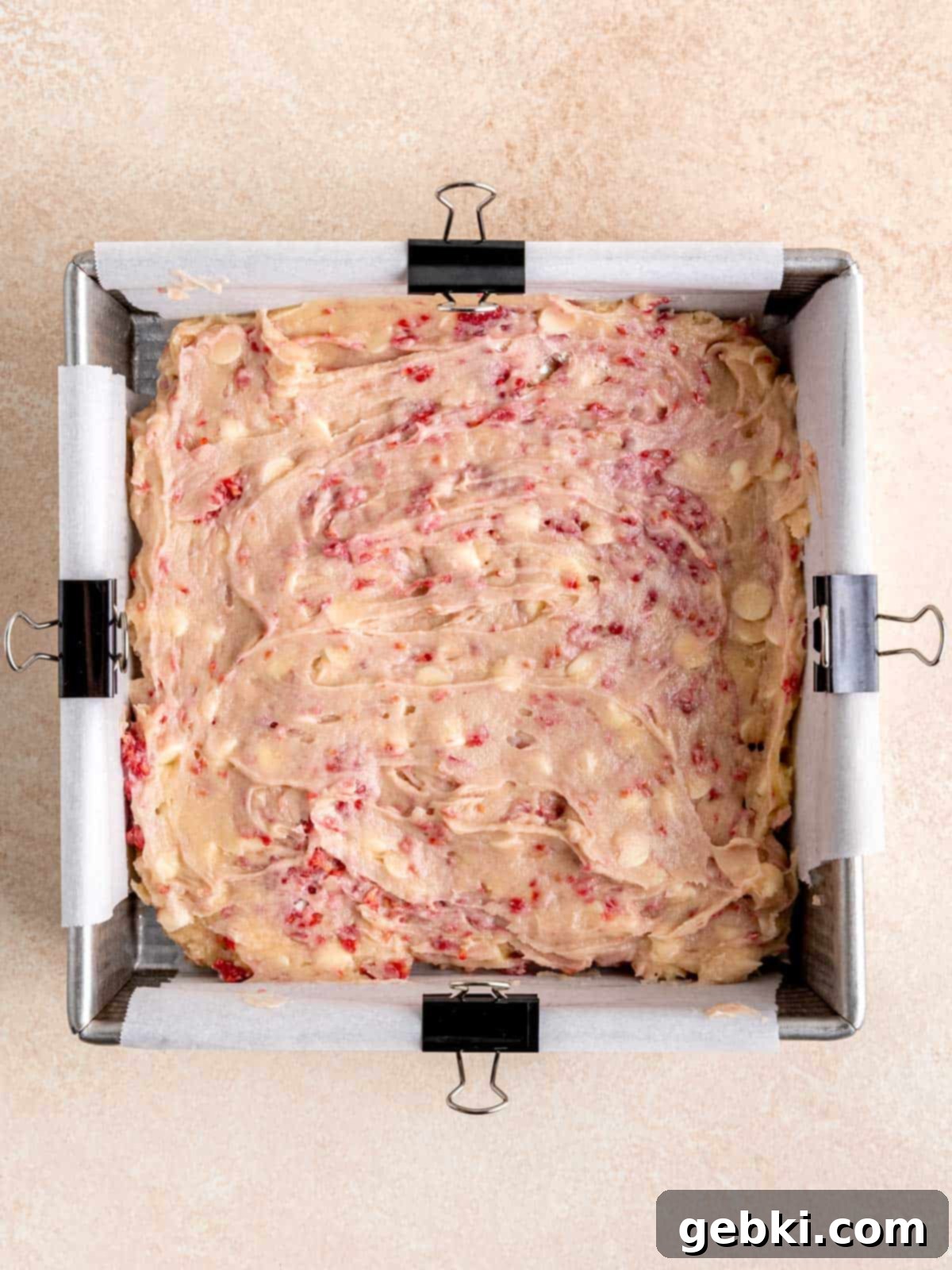 White Chocolate Raspberry Swirl Blondies 7 Smooth, rich white chocolate raspberry blondie batter spread evenly across the bottom of a parchment-lined square baking pan, ready for the oven.