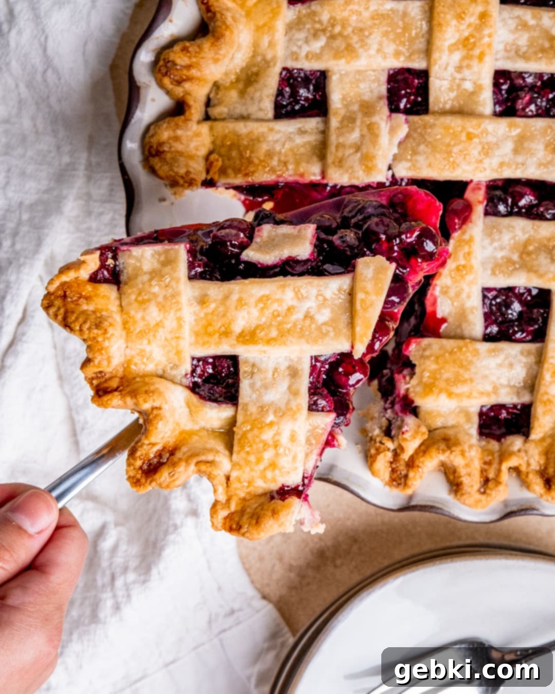 Aromatic Blueberry Delight 12 Lifting a perfect slice of spiced blueberry pie out of the pie dish, showcasing the juicy filling and flaky crust.