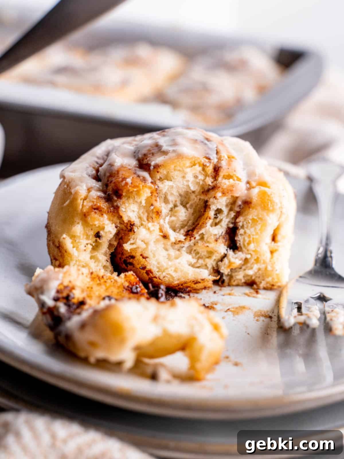 A frosted snickerdoodle roll on a plate with bites taken out of it, showing the soft interior.