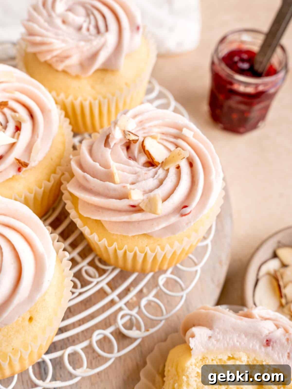 Fluffy almond cupcakes topped with vibrant raspberry cream cheese frosting and delicate sliced almonds, ready to be enjoyed.