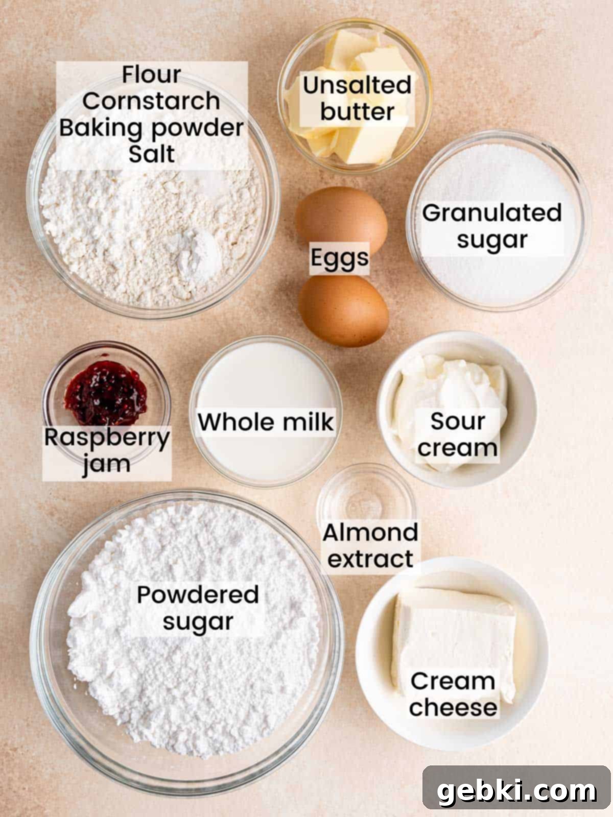 A selection of fresh, high-quality ingredients laid out, including almond extract, sour cream, whole milk, and raspberry jam, essential for making the almond cupcakes with raspberry cream cheese frosting.
