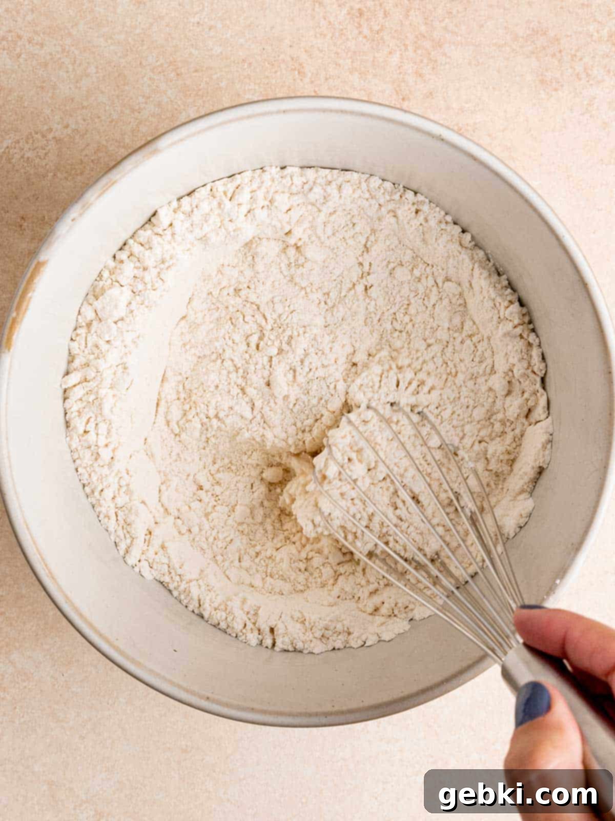 A bowl containing a light, fluffy mixture of flour, cornstarch, baking powder, and salt, being whisked together thoroughly to ensure even distribution of dry ingredients.