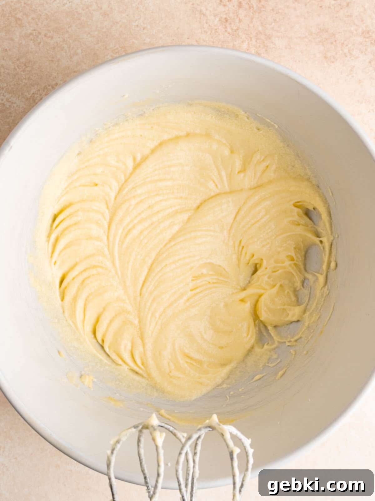 A creamy, pale yellow mixture of butter, sugar, eggs, almond extract, and sour cream, perfectly blended in a mixing bowl, showcasing the smooth base for the cupcake batter.