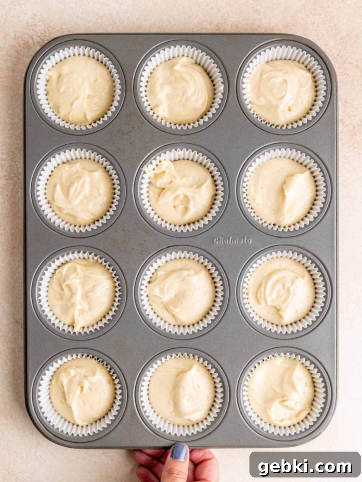 A muffin pan filled with cupcake liners, each neatly holding an equal portion of the smooth almond cupcake batter, ready for baking.