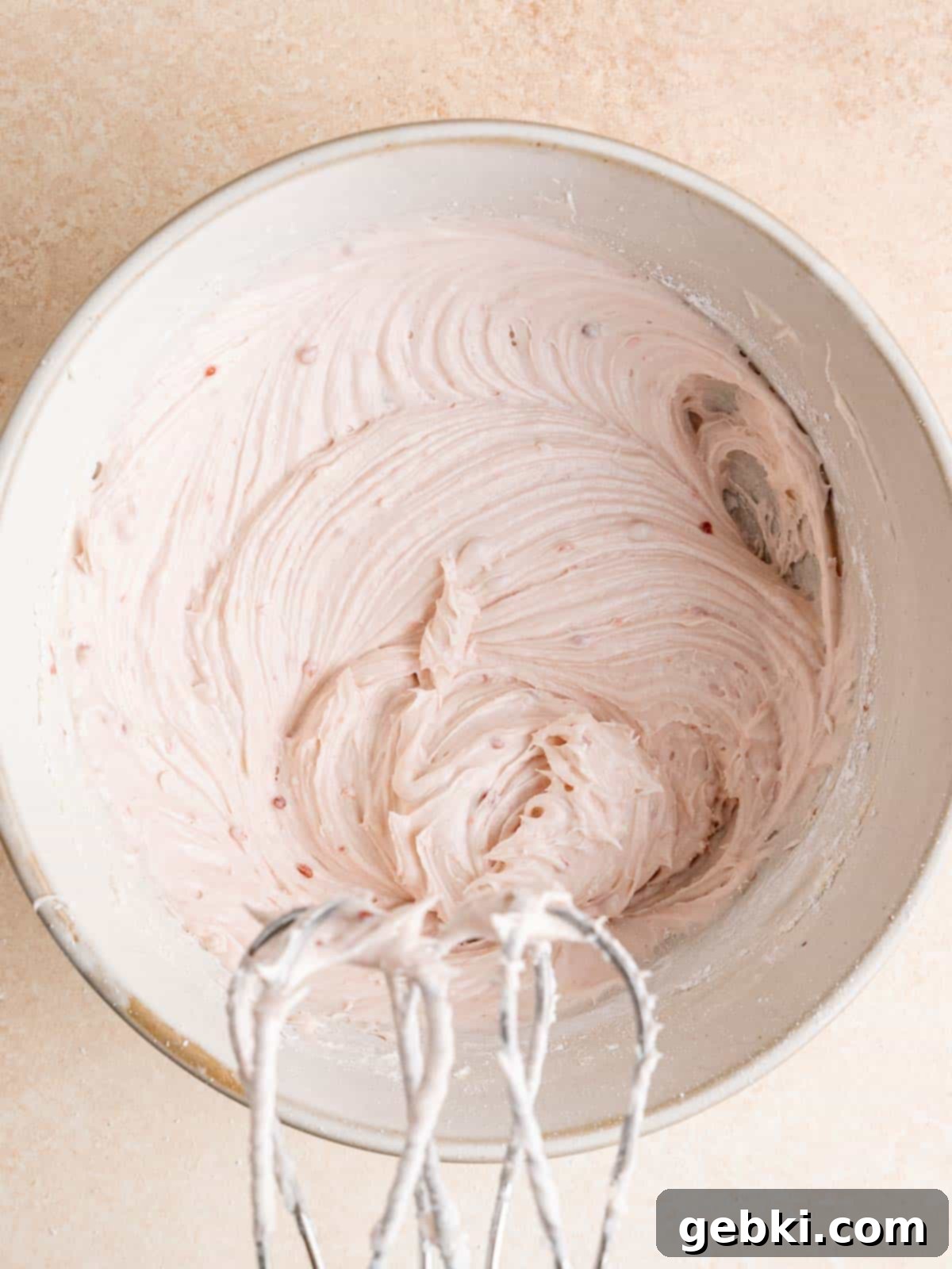 A bowl of smooth, pale pink raspberry cream cheese frosting, perfectly whipped and ready to be spread or piped onto cooled cupcakes.