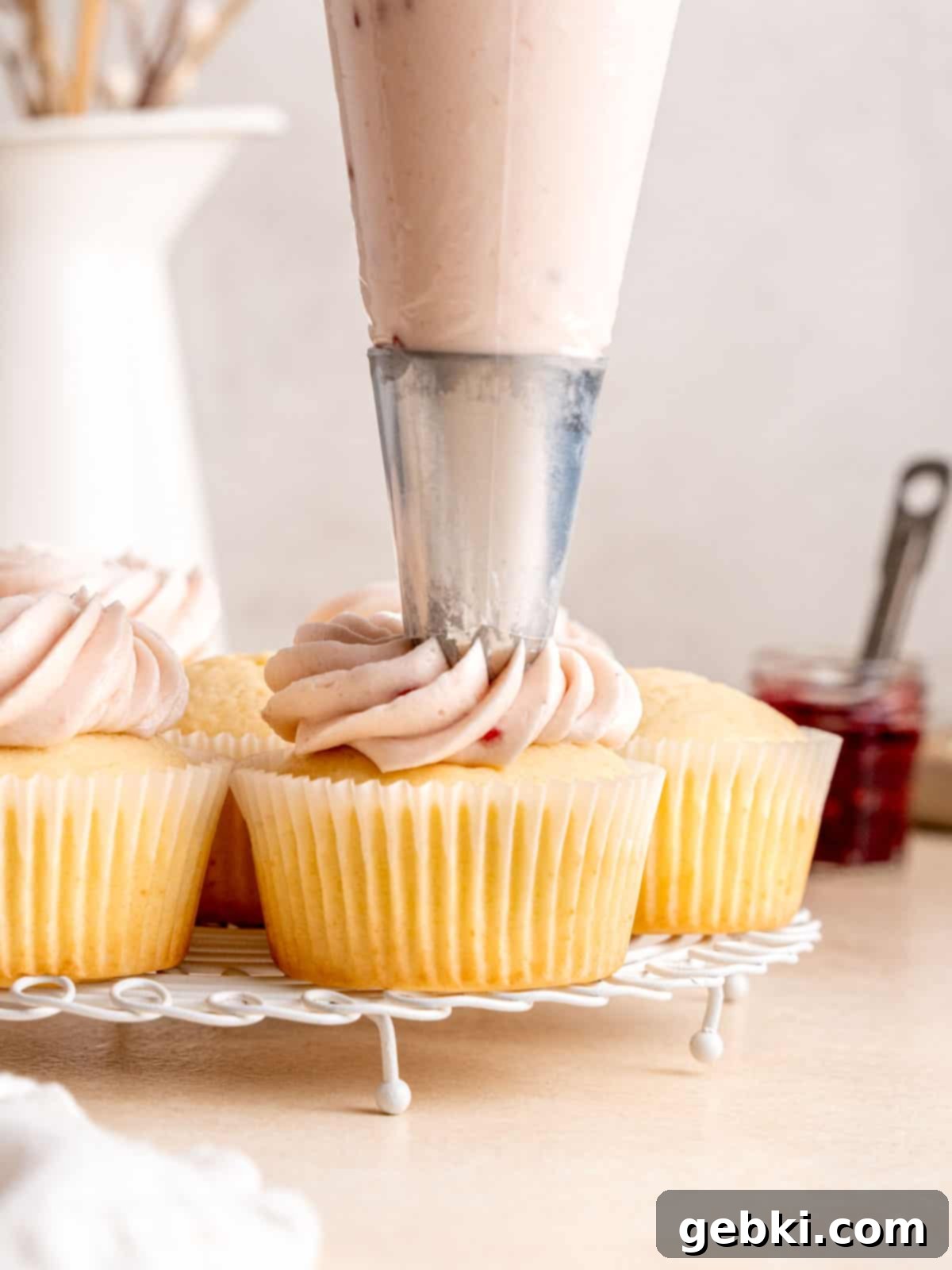 A beautifully piped swirl of raspberry cream cheese frosting on top of an almond cupcake, using a closed star piping tip for an elegant finish.