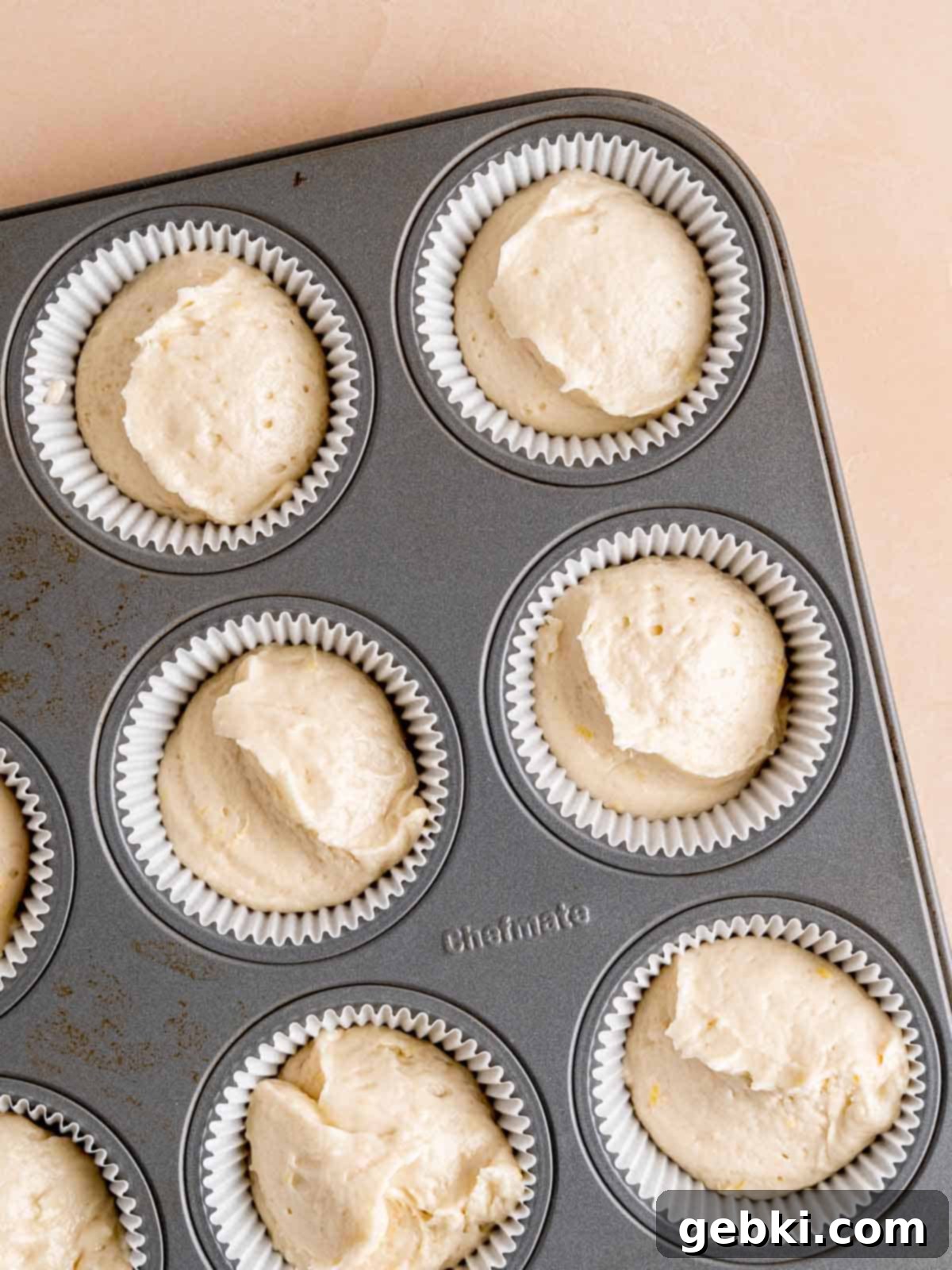 Zesty Lemon Cupcakes with Strawberry Filling 7 Cupcake liners in a baking pan, filled two-thirds with lemon cupcake batter, ready for baking.