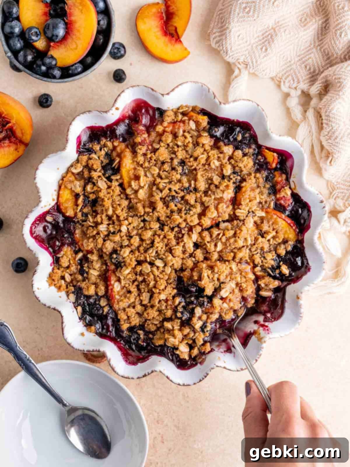 Sweet Summer Blueberry Peach Crisp 2 A hand holding a server inside a dish of homemade blueberry peach crisp, ready to be served.