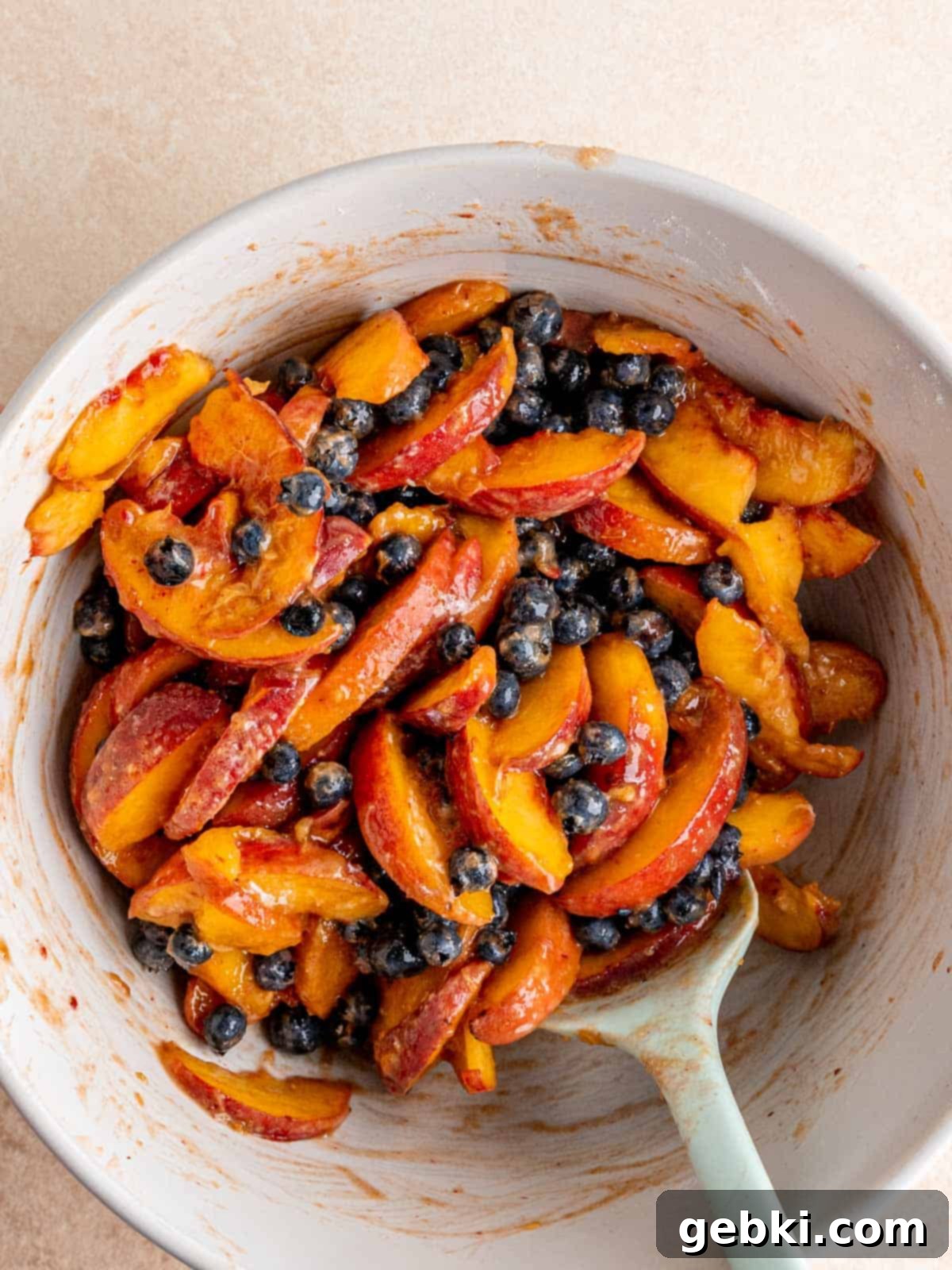 Sweet Summer Blueberry Peach Crisp 5 Fresh blueberries and sliced peaches mixed with flour, brown sugar, and lemon juice in a large bowl, creating the fruit filling for the crisp.