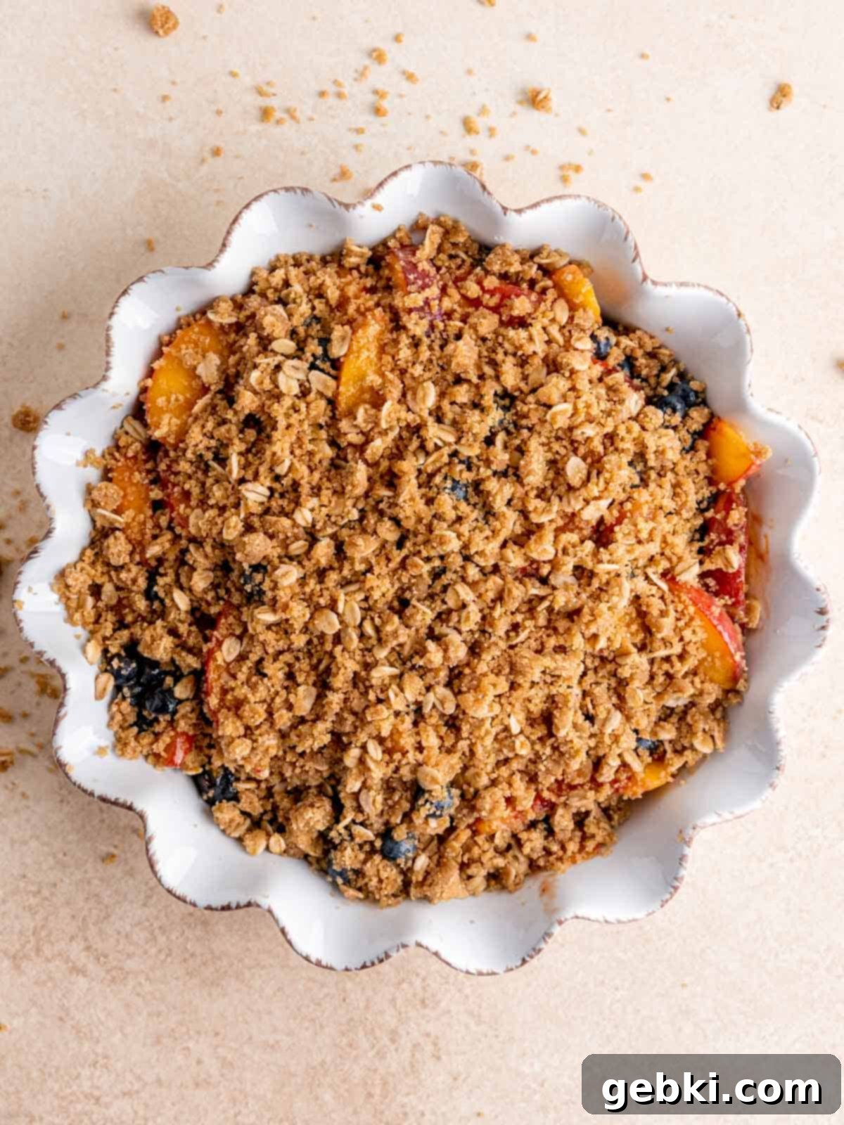 Sweet Summer Blueberry Peach Crisp 6 A pie dish filled with sweet blueberry peach fruit, topped with cinnamon oat streusel, ready for baking.