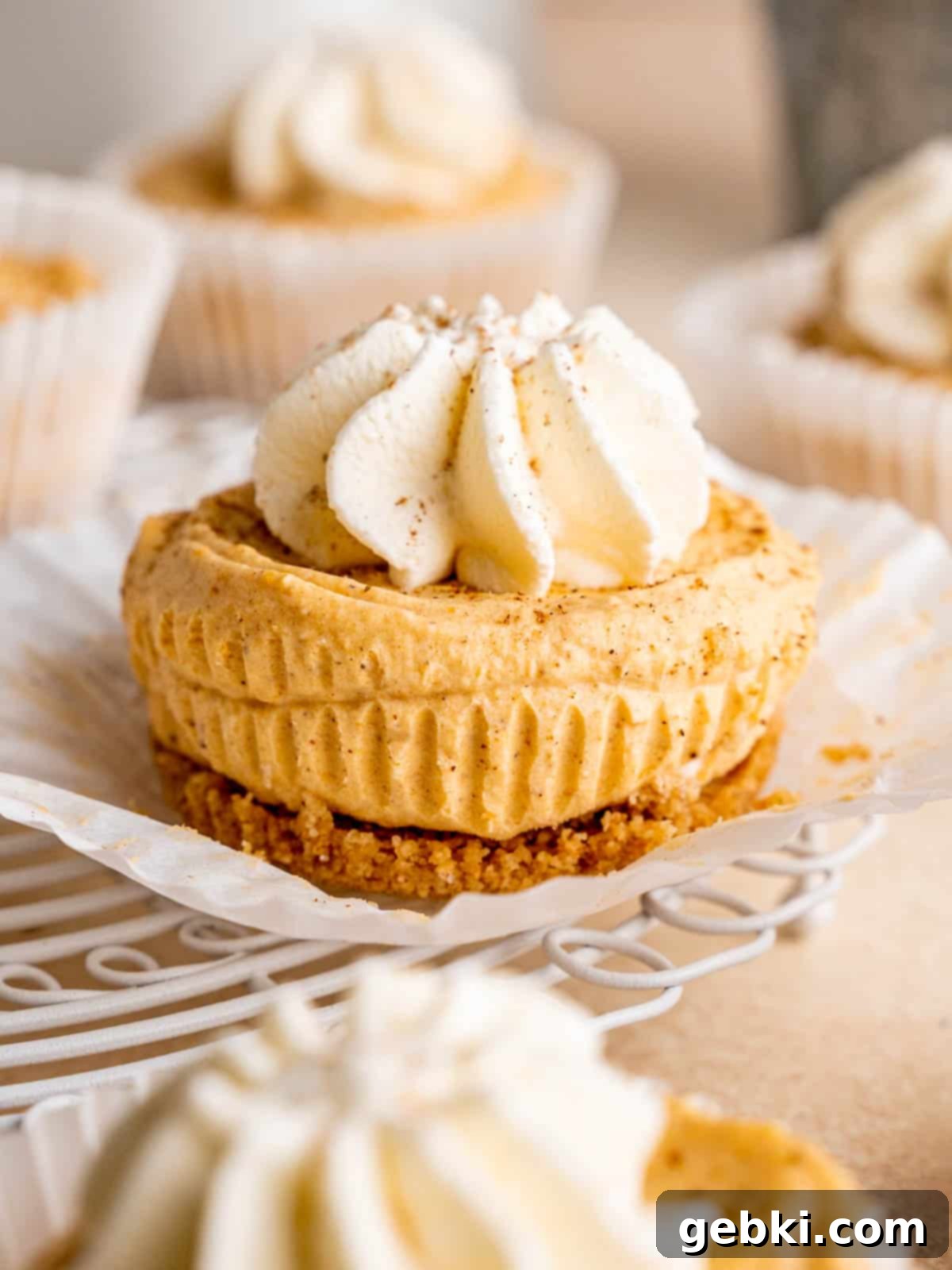 A mini pumpkin cheesecake with whipped cream sitting on a cupcake liner, ready to be enjoyed.