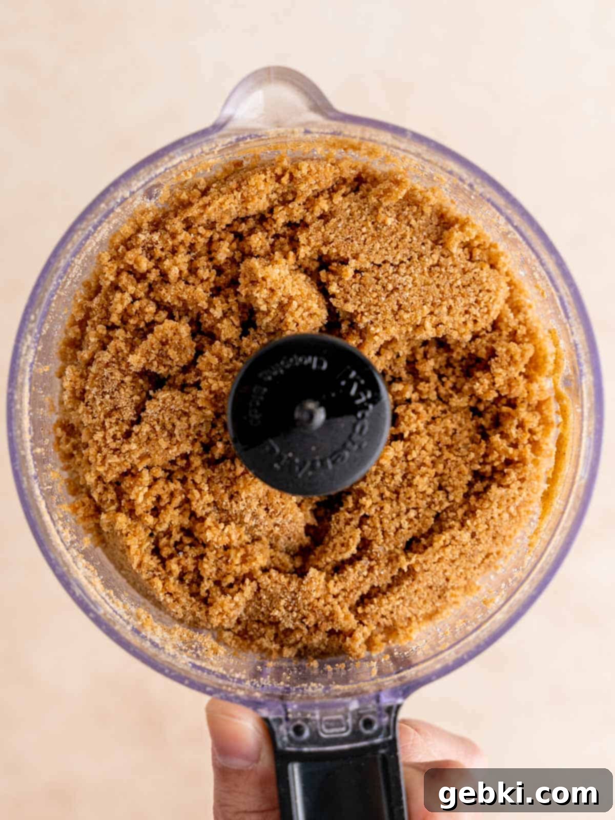Graham cracker crust mixture in a food processor, resembling wet sand.