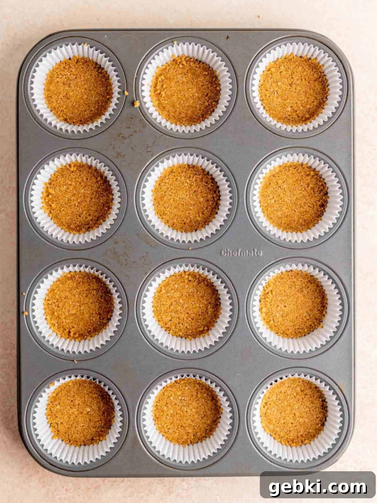 Graham cracker crust mixture pressed into the bottom of cupcake liners in a muffin tin.