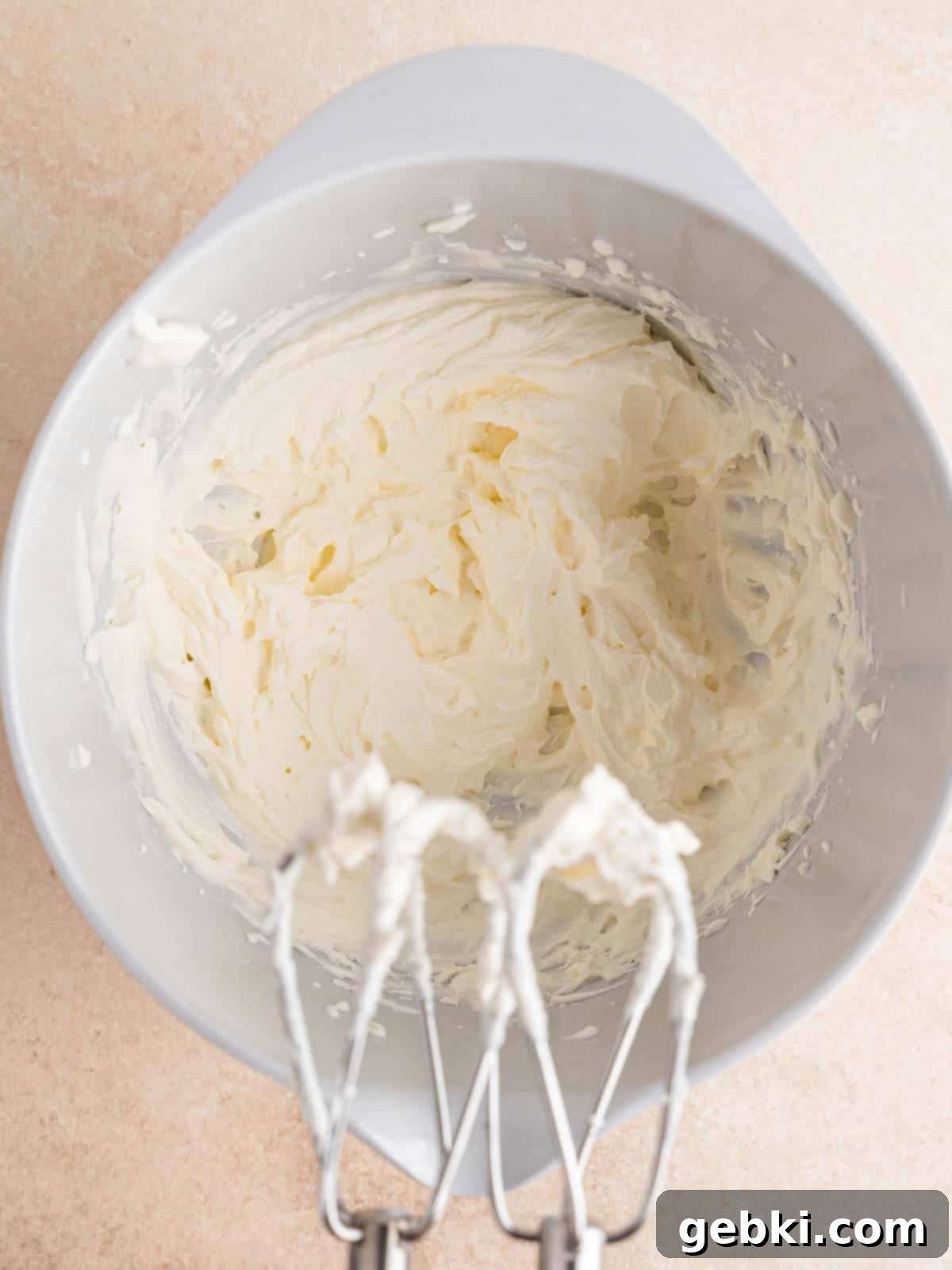 Heavy whipping cream being whipped to stiff peaks in a mixing bowl with a hand mixer.