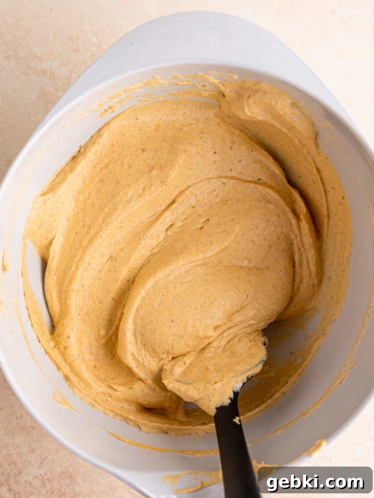 Folding whipped cream into pumpkin cheesecake mixture with a spatula.