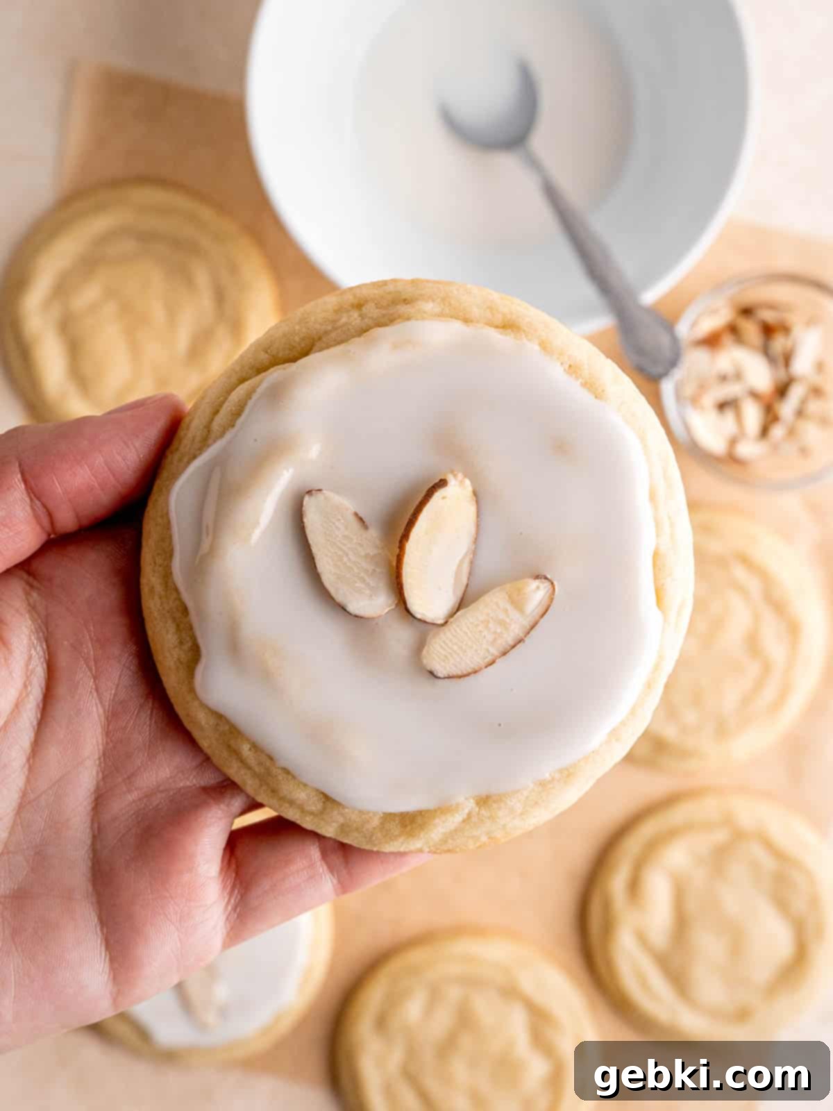 Velvet Almond Sugar Cookies 8 A hand holding an almond cookie with icing and sliced almonds on top.