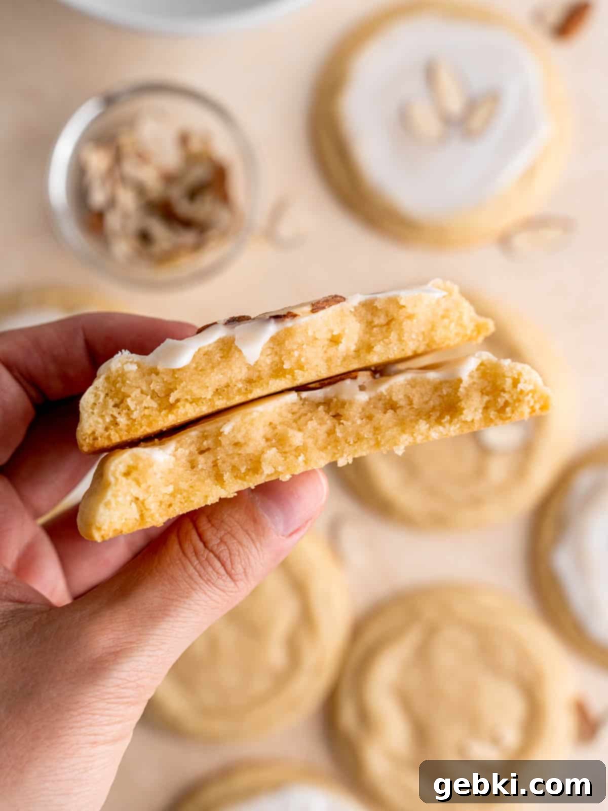 Velvet Almond Sugar Cookies 9 A hand holding two halves of a soft iced almond cookie.