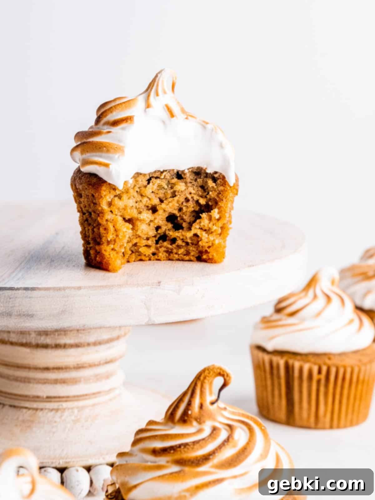 A sweet potato cupcake with toasted meringue frosting sitting on a cake stand with a bite taken out of it.