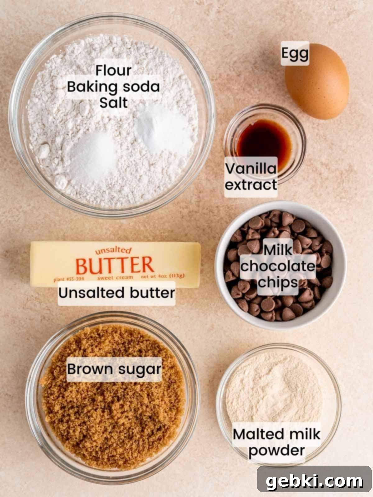 Ingredients laid out for making chewy malted chocolate chip cookies, including malted milk powder, butter, sugar, flour, and chocolate chips.