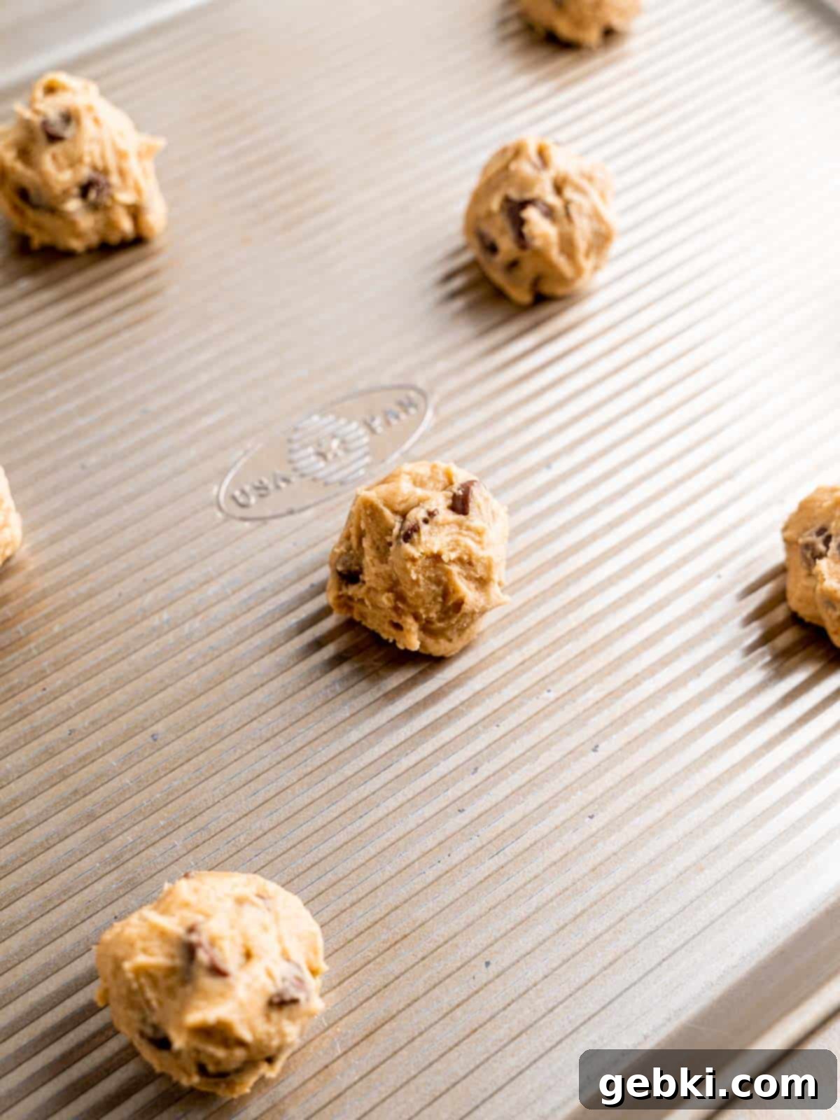 Perfectly scooped chocolate chip cookie dough balls arranged on a parchment paper lined baking sheet.