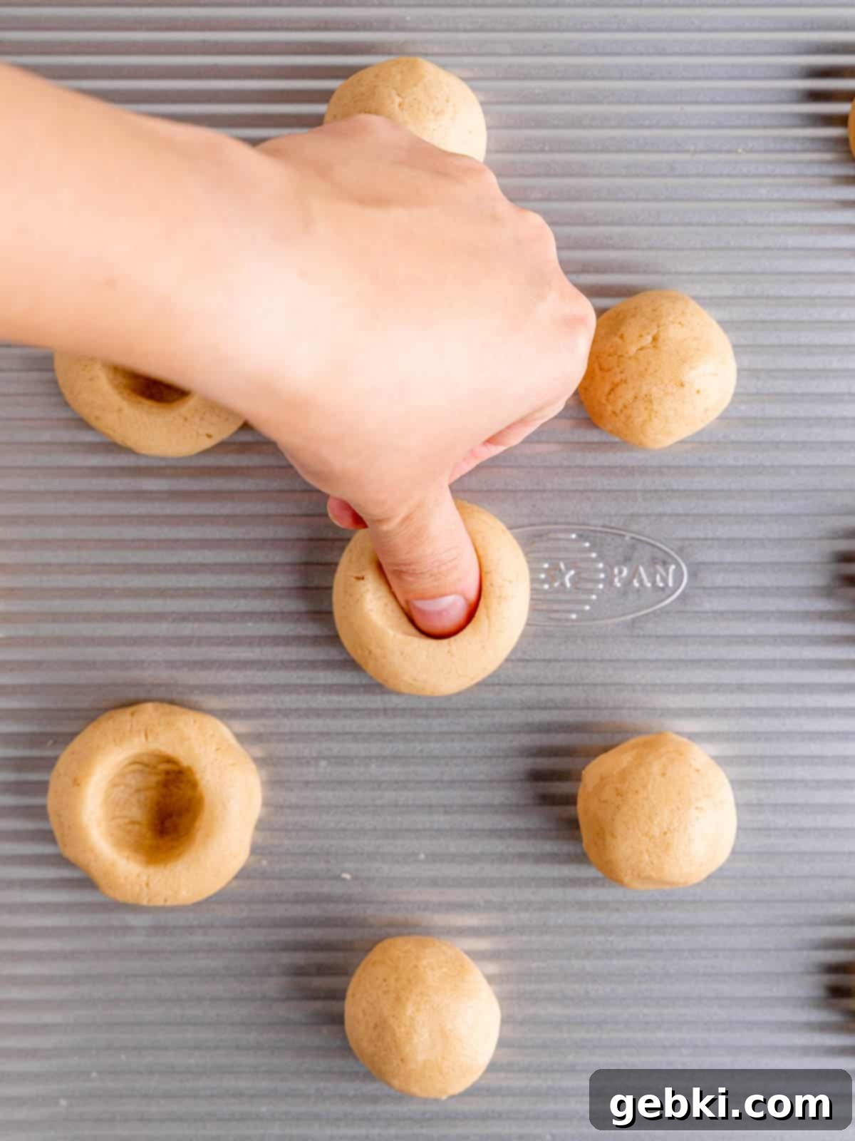 Making an indent in the center of a cookie dough ball with a thumb.