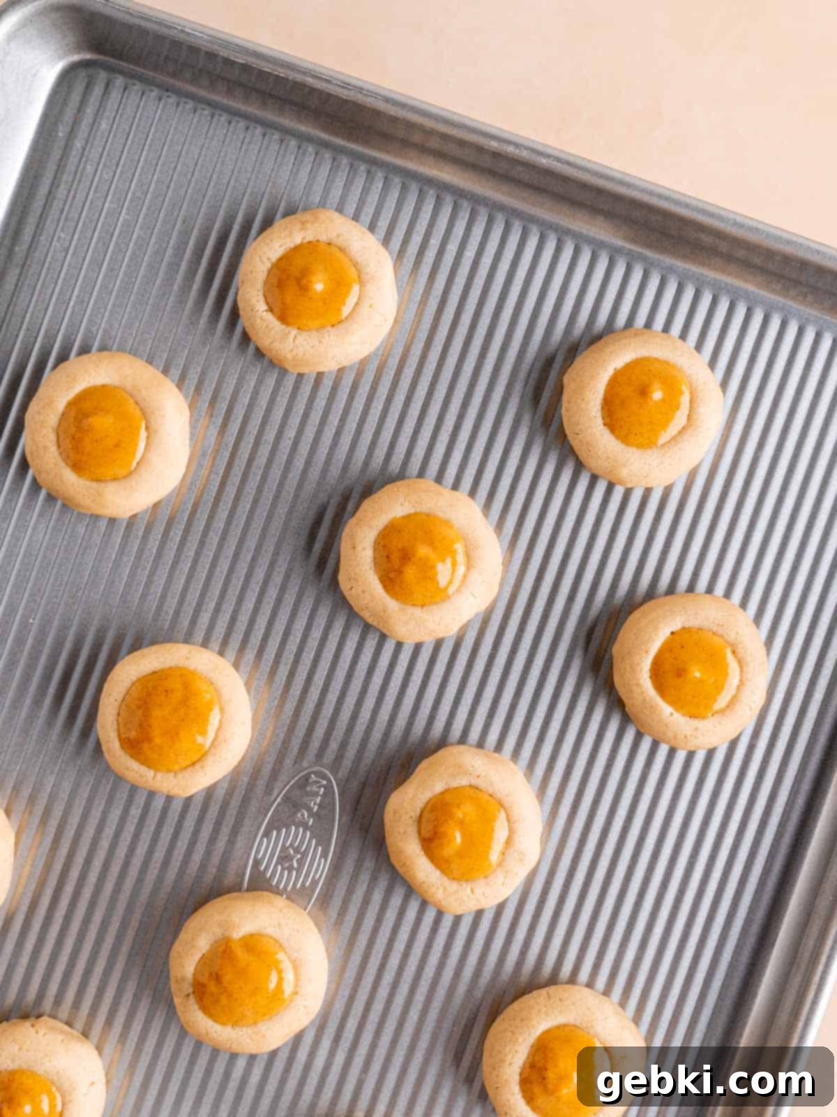 Thumbprint cookies with pumpkin pie filling on a baking sheet.