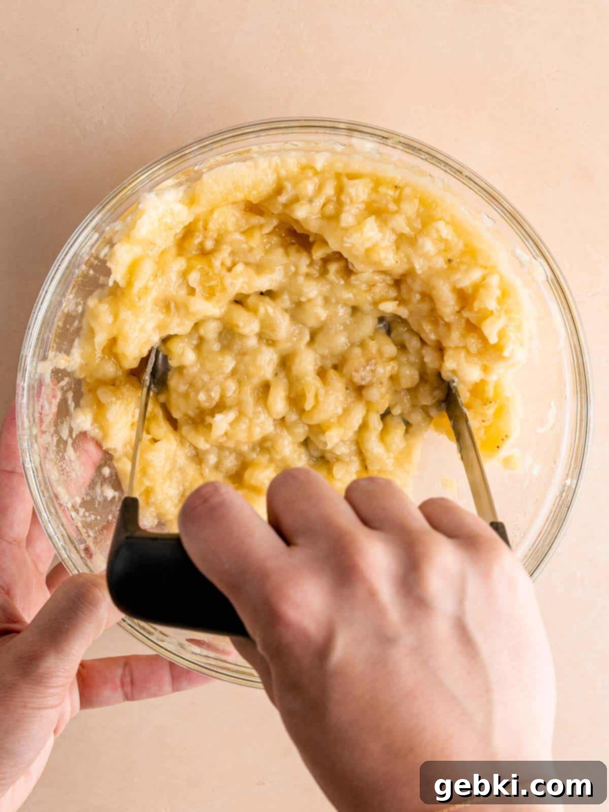 Golden Honey Banana Loaf 4 A person mashing overripe bananas in a medium-sized bowl with a fork, showing their dark, spotty peels.