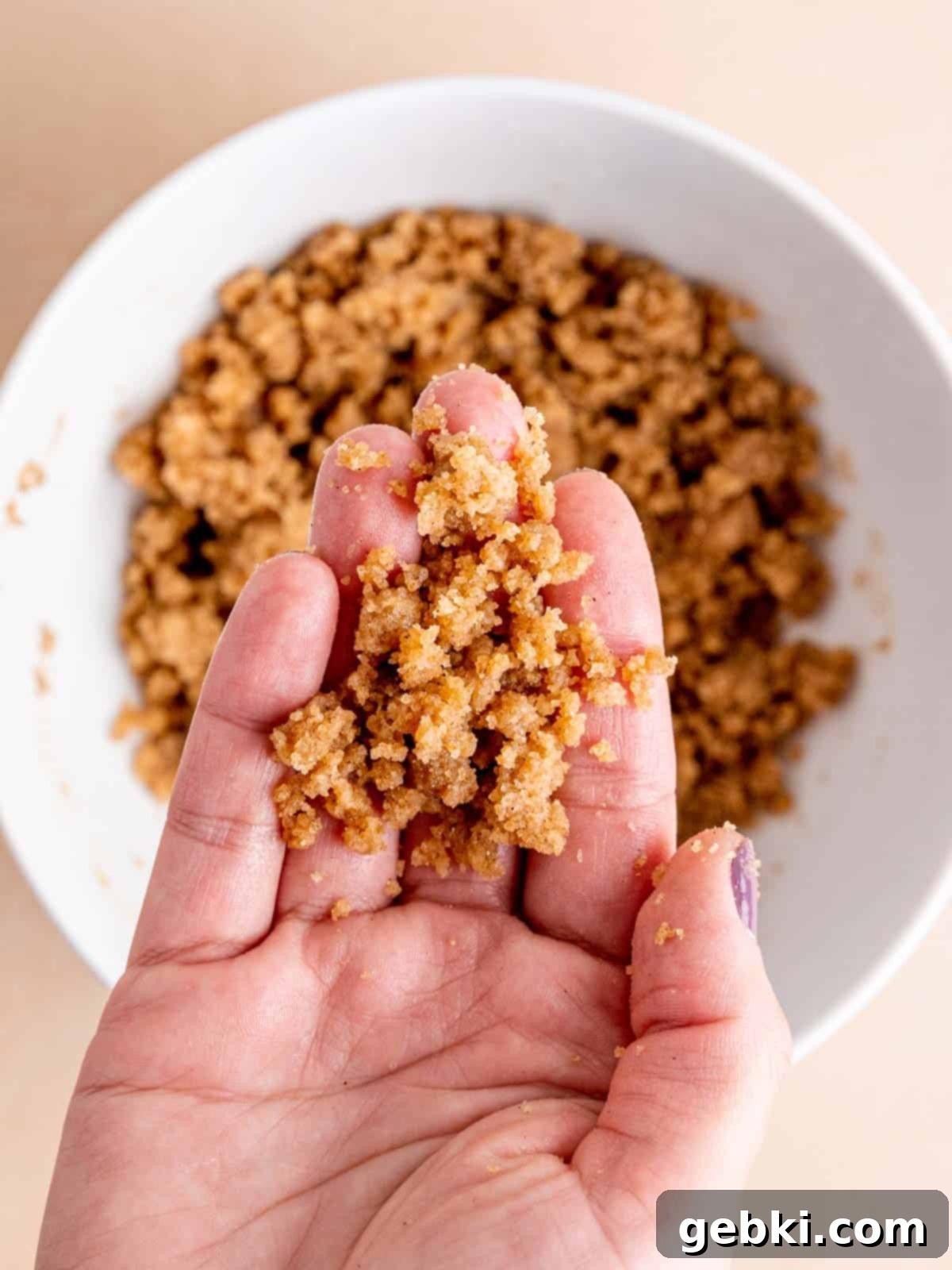 A hand holding cinnamon streusel crumb topping.