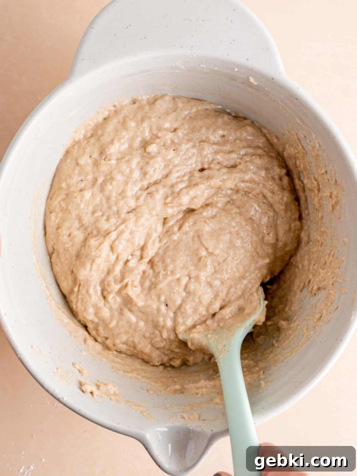 Folding dry muffin ingredients into a bowl of wet ingredients using a spatula.