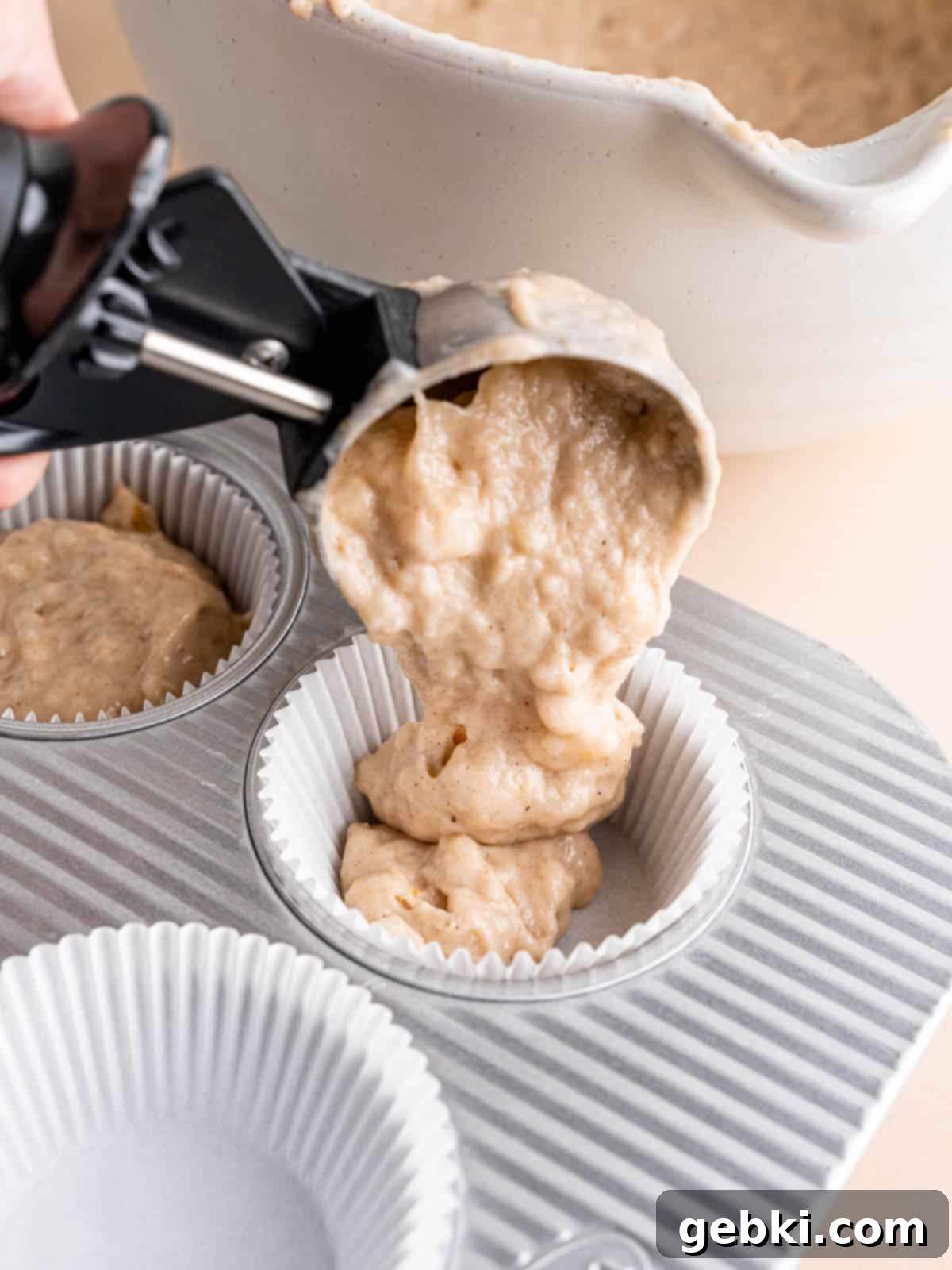 Adding batter to muffin liners in a muffin pan with an ice cream scoop.