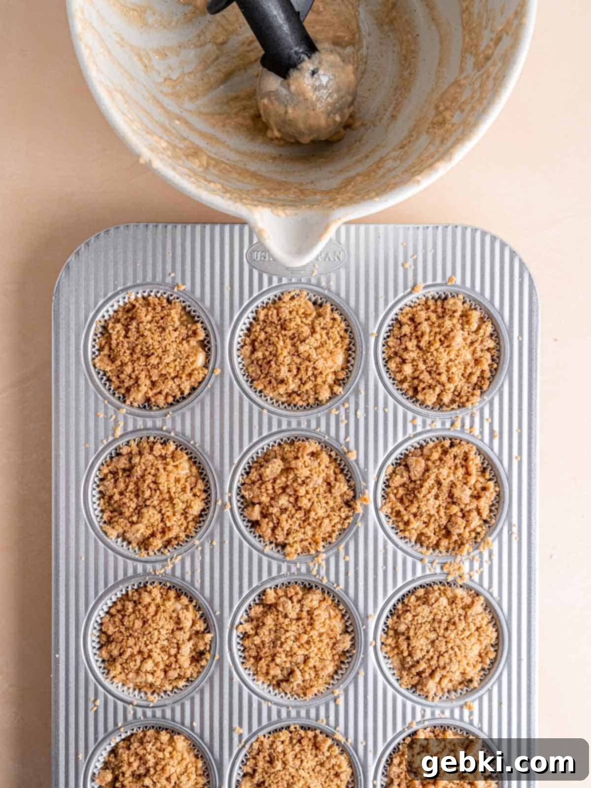 A muffin pan filled with honey pear muffin batter topped with streusel.