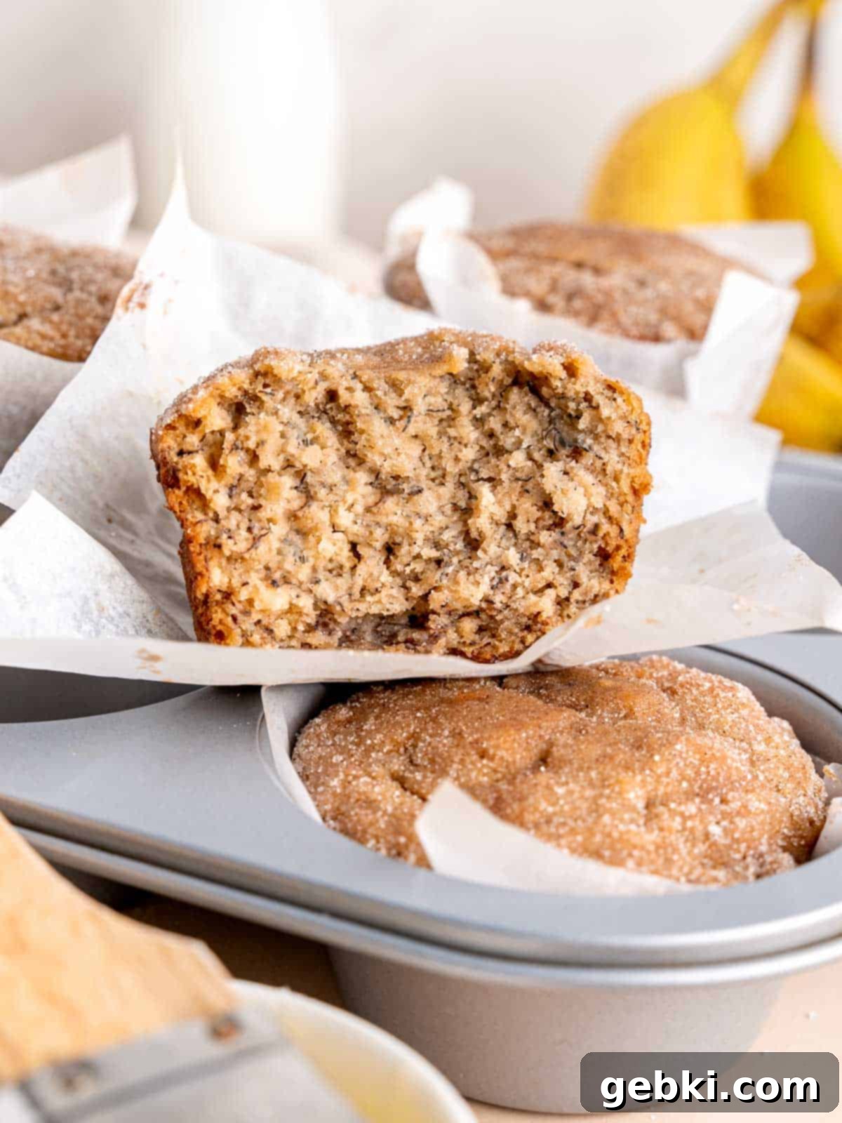 Cinnamon Swirl Banana Bread Muffins 2 Half of a cinnamon banana bread muffin on a muffin tin, showcasing its soft interior and crunchy topping.