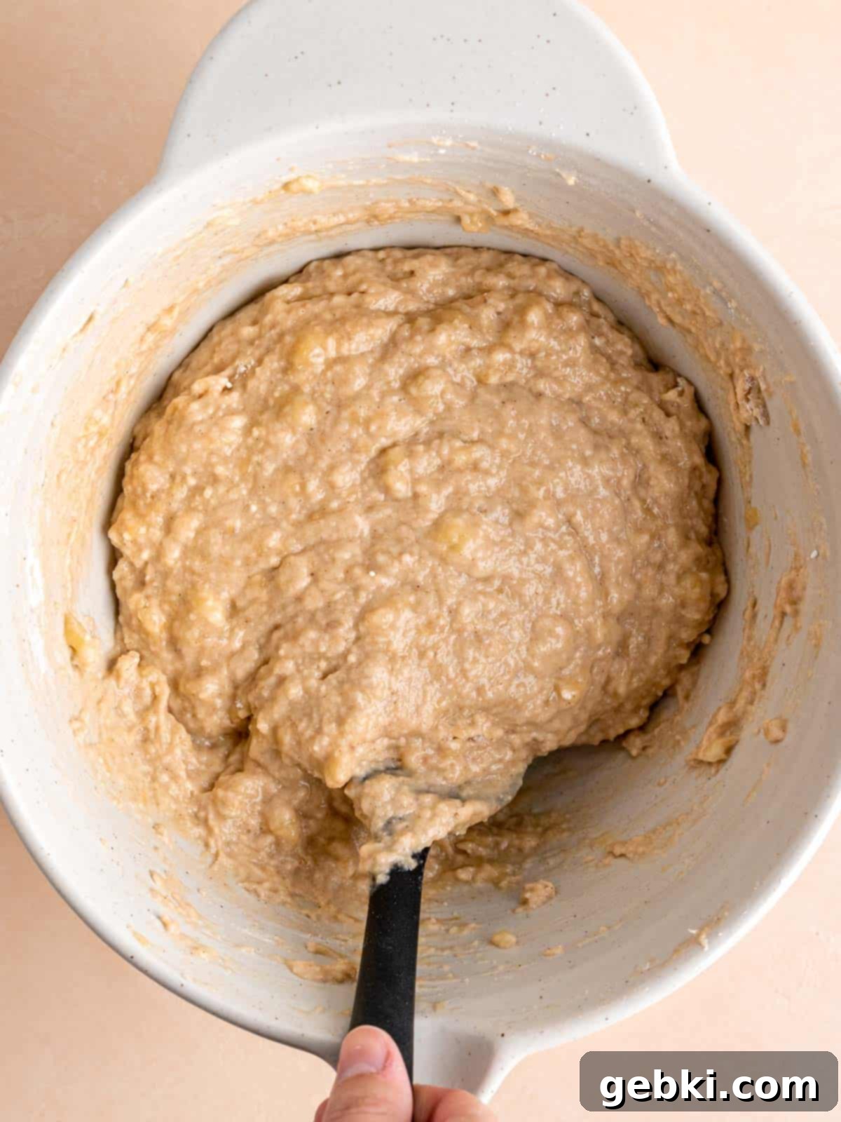 Cinnamon Swirl Banana Bread Muffins 6 Mixing cinnamon banana bread batter in a bowl with a spatula, showing the combined wet and dry ingredients.